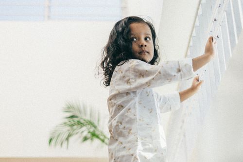 Free A young girl with curly hair stands indoors, wearing white clothes and looking back. Stock Photo