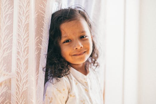 Portrait of a Little Brunette Girl Standing by a Window