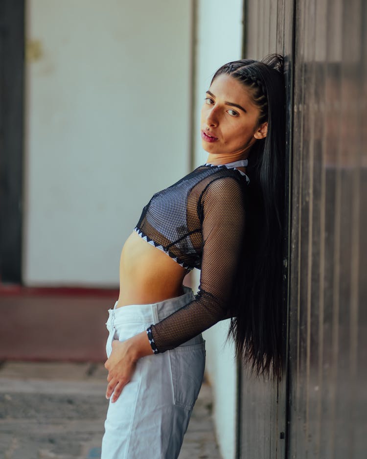 Young Brunette Woman In Black Mesh Crop Top Posing By A Wall