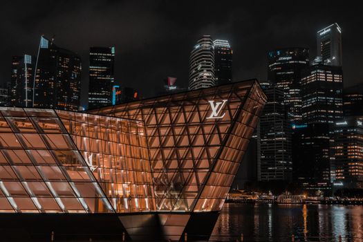 Captivating night view of Singapore skyline with iconic Louis Vuitton architecture reflected on water.