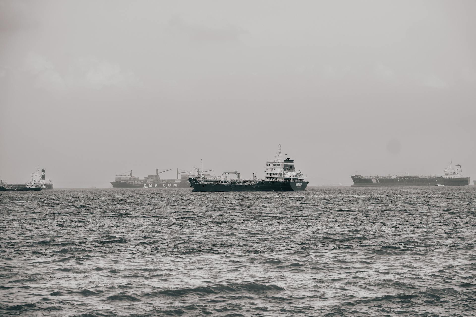 A serene shot of cargo ships cruising through calm, foggy waters in an industrial maritime setting.