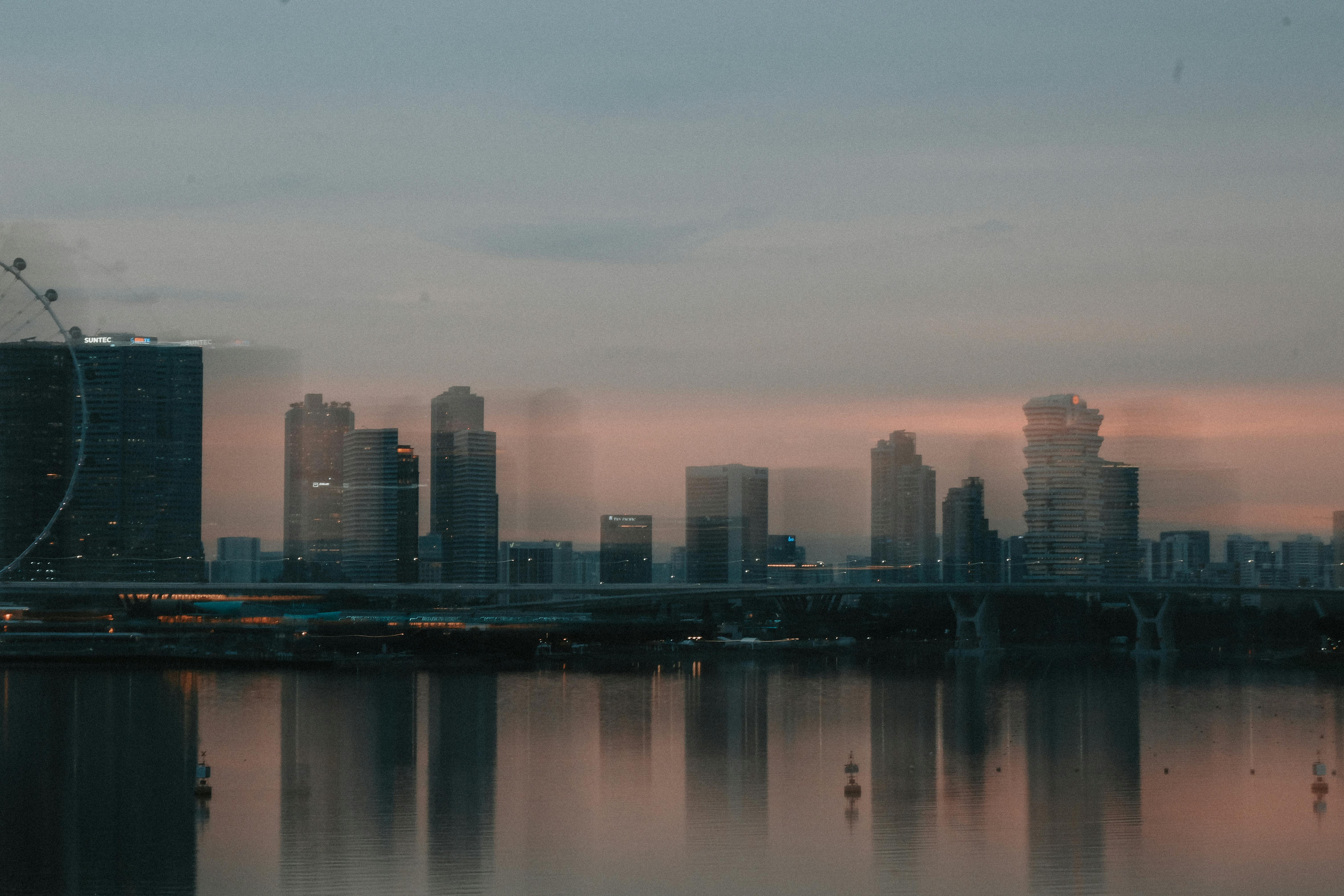 A moody cityscape of Singapore's skyline at dusk with reflective waters and dark clouds.