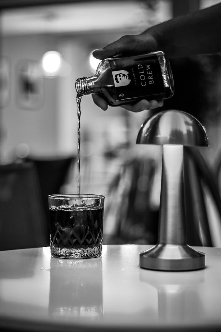 Black And White Photo Of A Man Pouring Cold Brew Coffee Drink From A Bottle