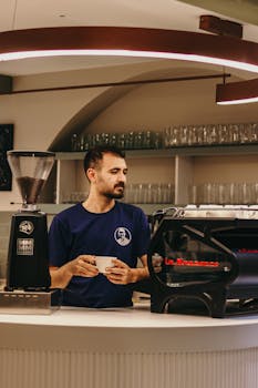 A barista in a modern cafe holds a cup while using advanced coffee equipment.