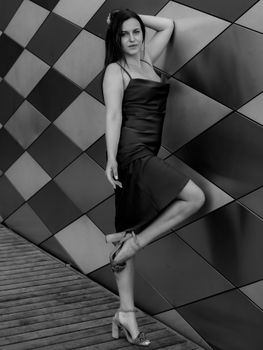 Black and white photo of a woman posing in a chic dress and heels against a modern geometric wall.