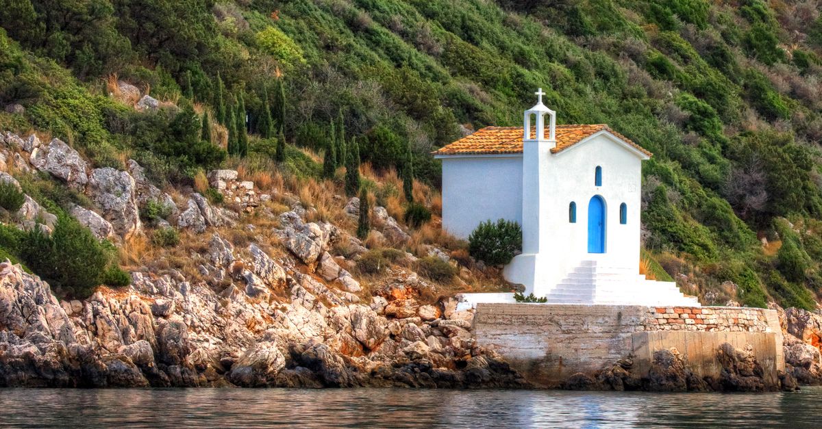 A scenic view of a charming white church with a blue door nestled by the sea in Ithaca, Greece.