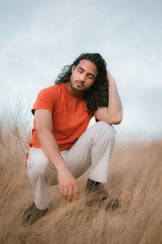 A young man in an orange t-shirt kneels with serenity in a Venezuelan field.