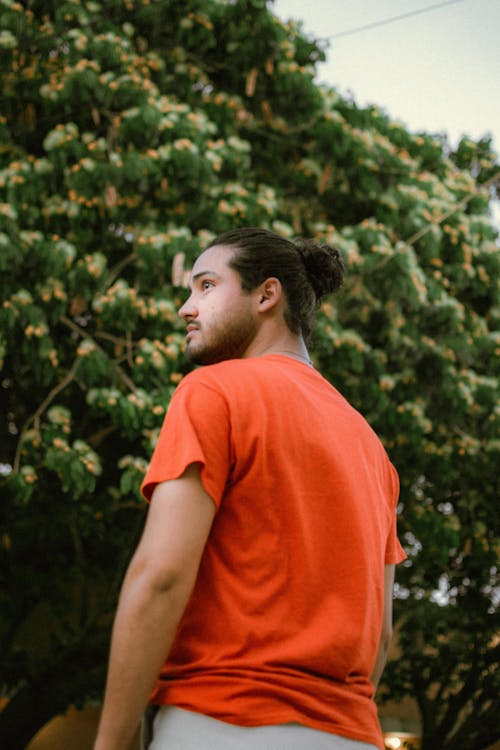 Low Angle Shot of a Man in an Orange T-shirt Standing on the Background of Trees