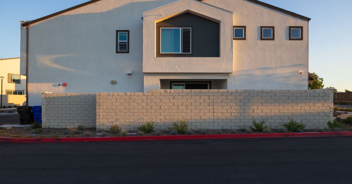 Front view of a modern house with a brick wall and minimalistic design under clear skies.