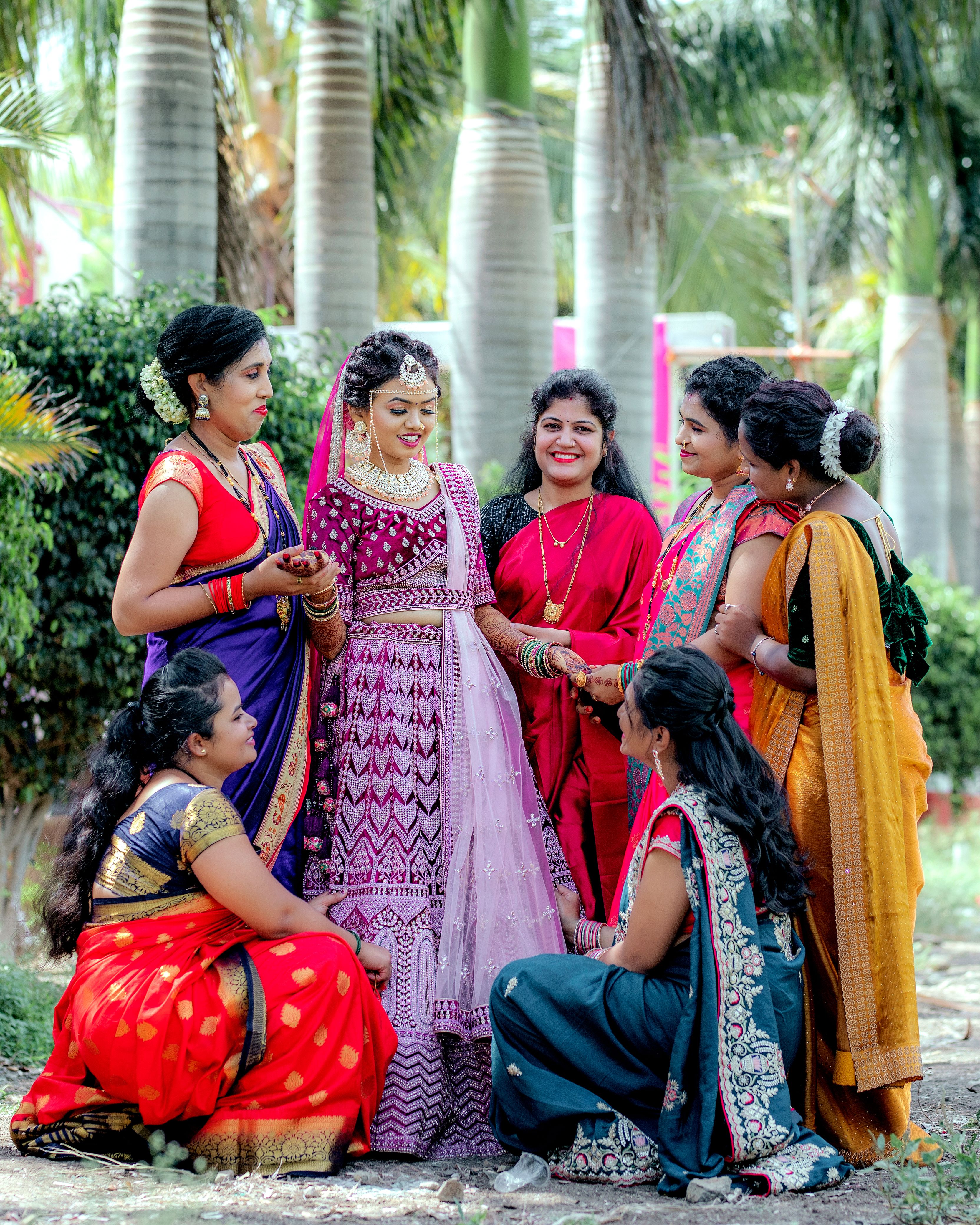 Beautiful Indian bride surrounded by bridesmaids in vibrant attire at an outdoor ceremony.