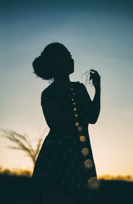 Artistic silhouette of a woman with bokeh lights during sunset, creating a moody and dreamy atmosphere.