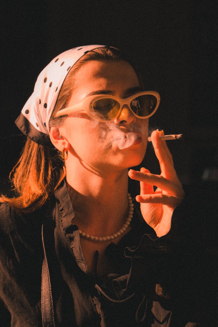 Woman In Black Shirt And White Polka Dot Headscarf Smoking A Cigarette