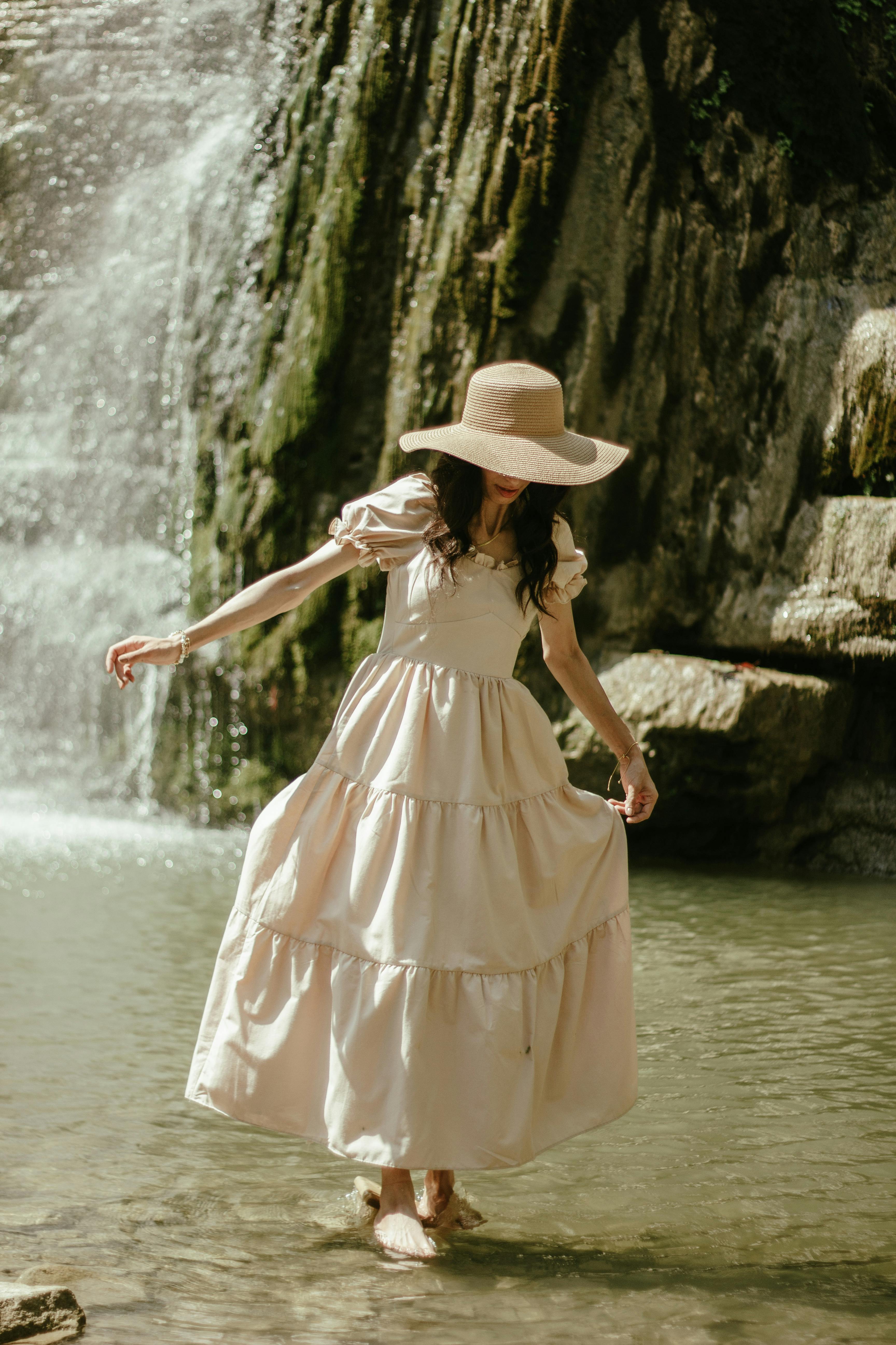 A person in a dress and hat standing in water
Description automatically generated