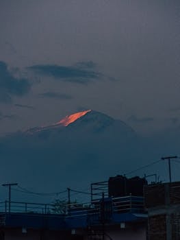 A stunning view of a mountain peak illuminated by the setting sun, partially obscured by clouds.
