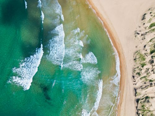 Free Breathtaking aerial view of turquoise ocean waves gently crashing onto a pristine sandy beach. Stock Photo