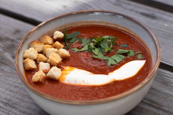 Deep red tomato soup with sour cream swoosh, croutons and parsley in ceramic bowl