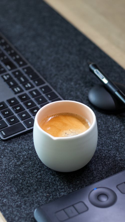 Close-up of a Cup of Coffee Standing next to a Keyboard 