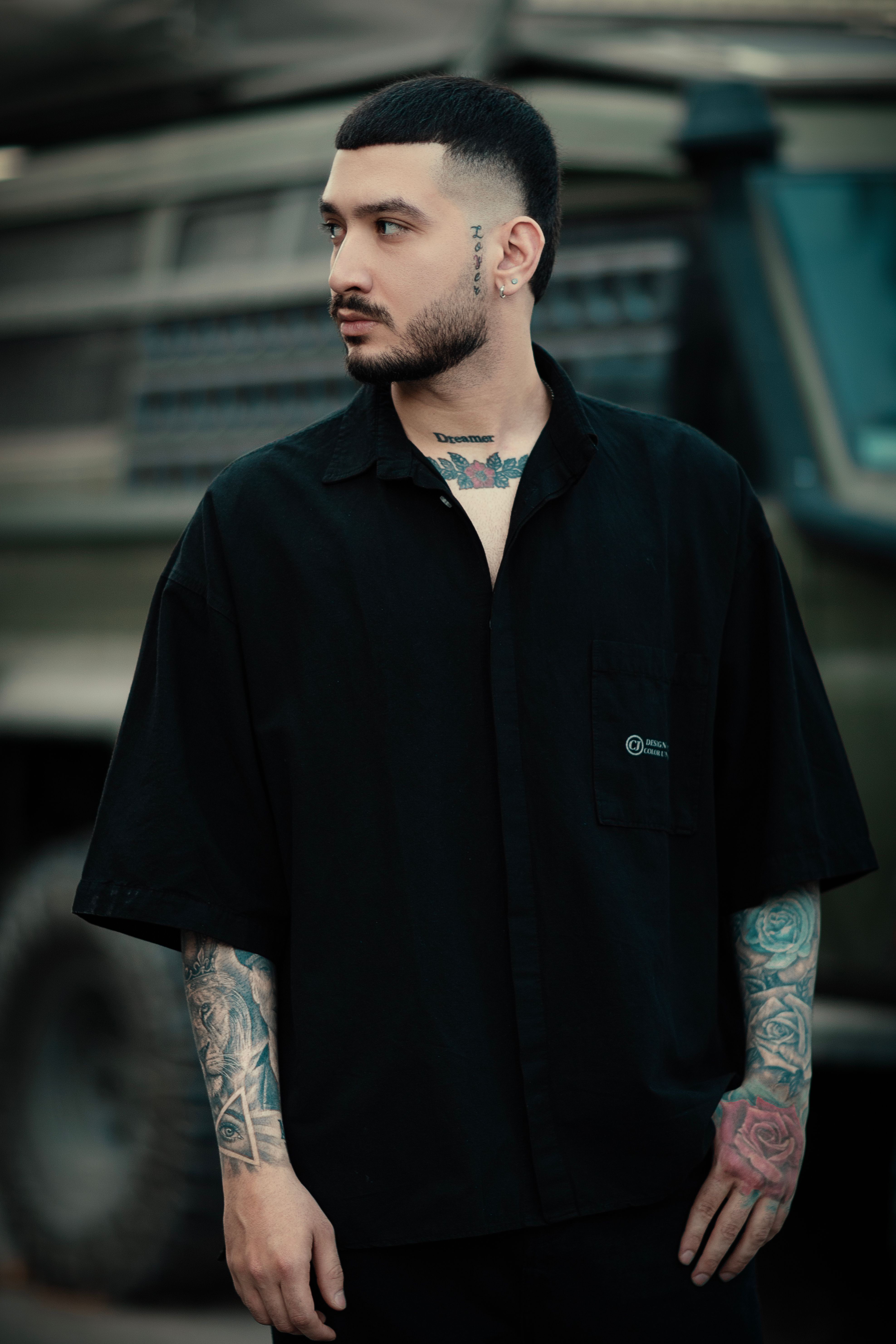 Portrait of a tattooed man in casual attire with an urban background.