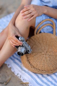 Close-up of a woman holding a camera while sitting on a beach blanket, capturing summer vibes.