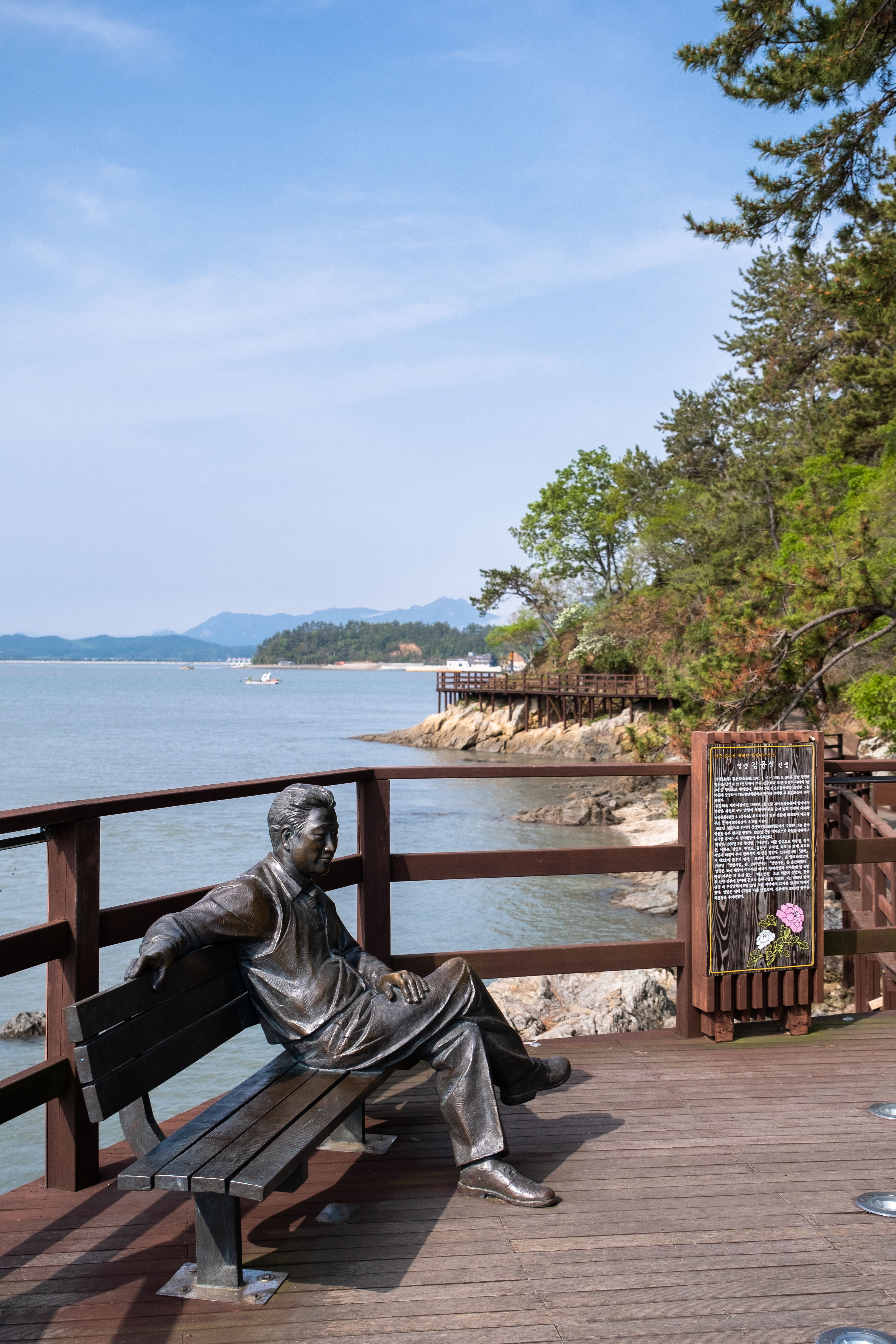 Statue resting on a lakeside bench along a scenic boardwalk, surrounded by nature.