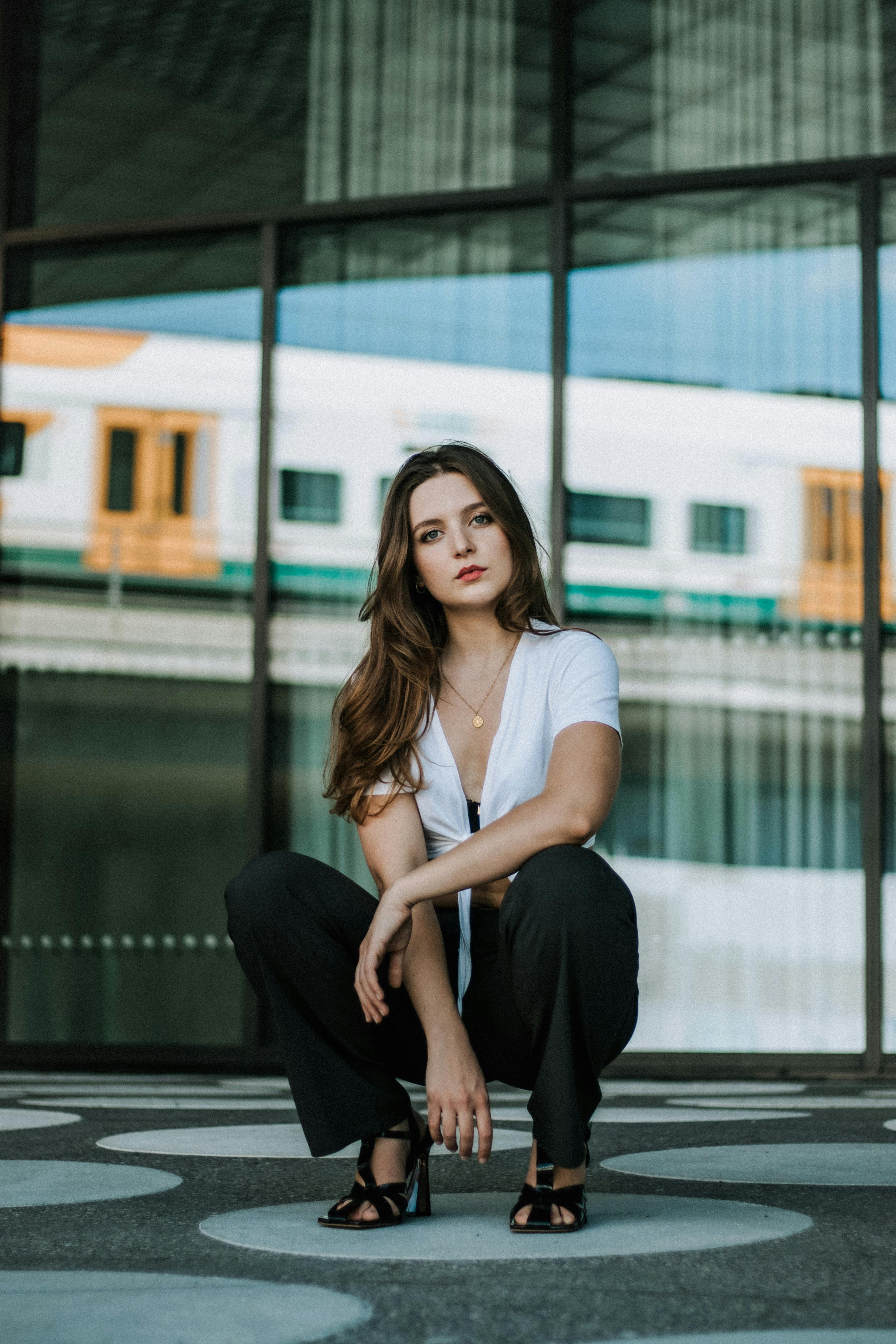 Stylish young woman crouching in an urban setting, exuding confidence and style.
