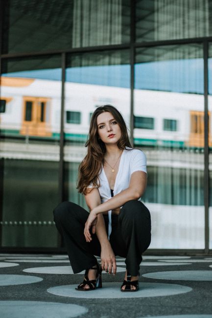 Stylish young woman crouching in an urban setting, exuding confidence and style.