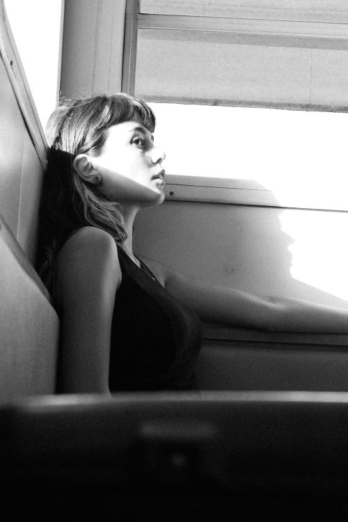 Free Black and white portrait of a young woman sitting by a window, lost in thought. Stock Photo