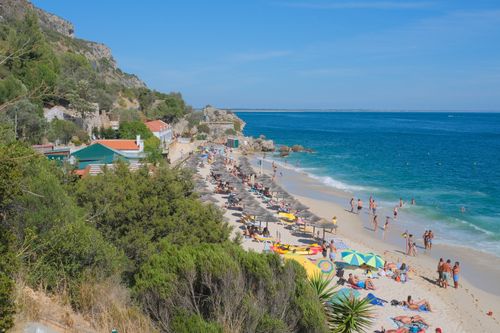 Free A bustling summer day at Portinho da Arrábida beach with sunbathers and umbrellas along the shore. Stock Photo