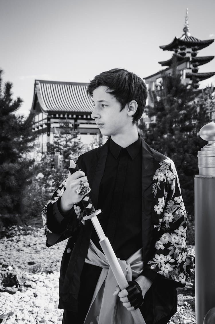 Boy In A Kimono Drawing A Katana Standing In The Garden Of A Traditional Japanese House