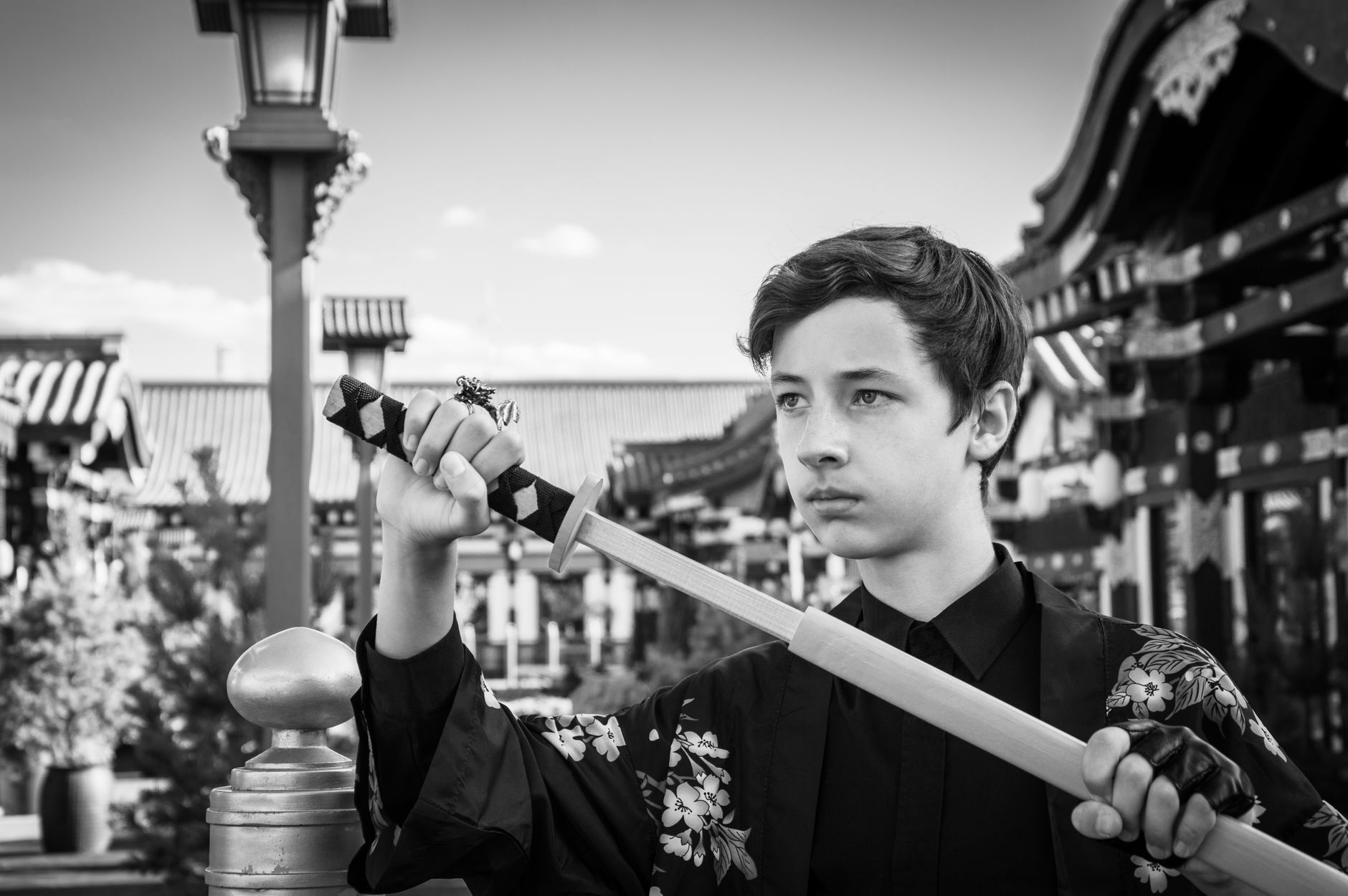 Black and white portrait of a teenage boy in a kimono holding a katana sword, evoking Japanese culture.