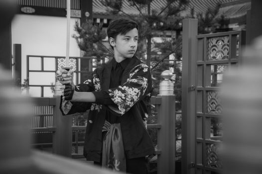 A teenager poses holding a katana in traditional attire, exuding samurai vibes.