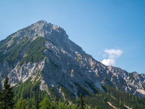 Free Breathtaking view of a rocky mountain peak with lush green forests under a clear blue sky. Stock Photo