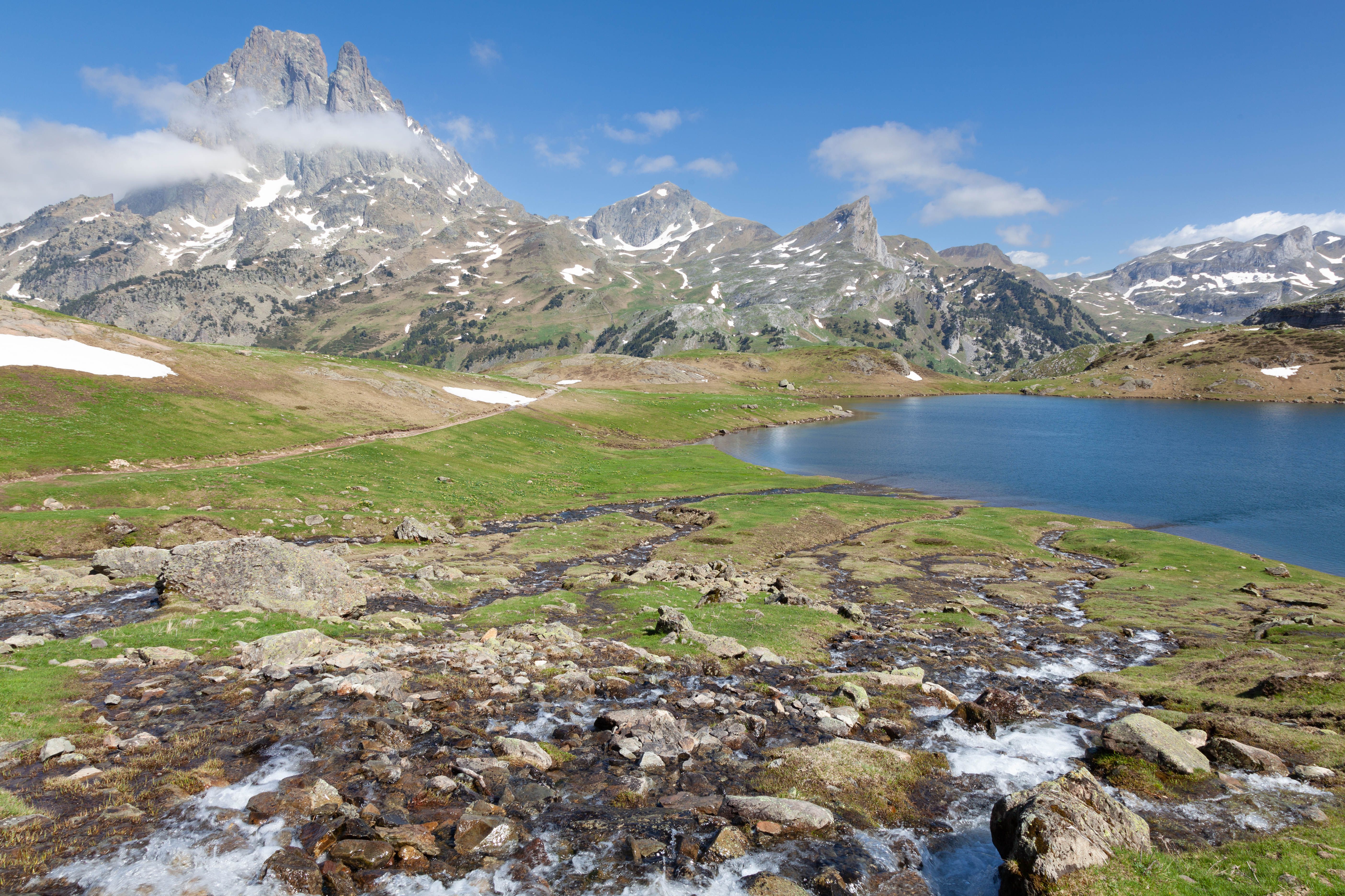 A mountain lake surrounded by grass and rocks · Free Stock Photo