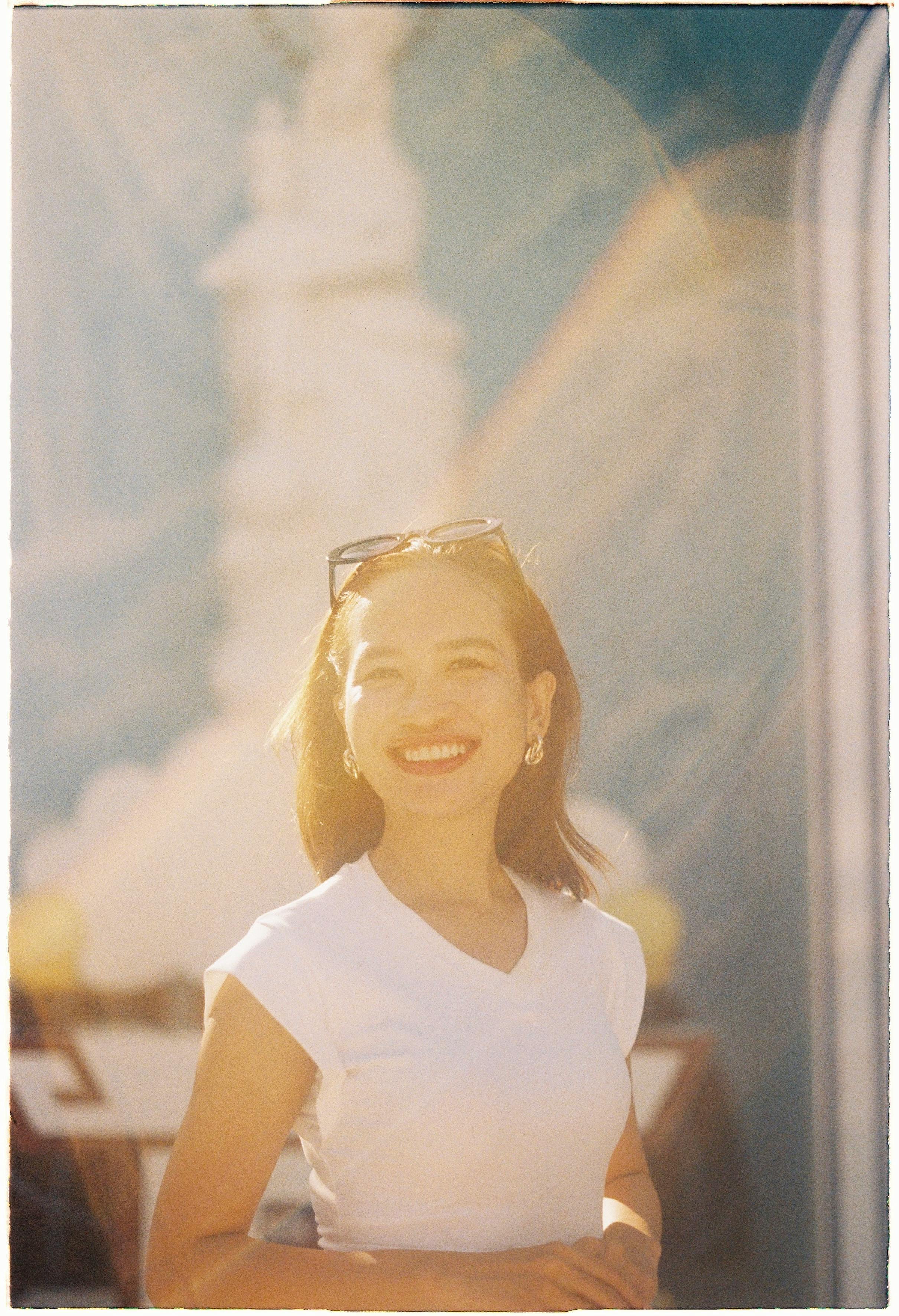 A cheerful woman smiling in a sunlit portrait with a soft background.