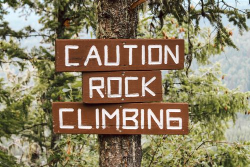 Free Wooden warning sign on a tree cautioning about rock climbing, set in a forest. Stock Photo