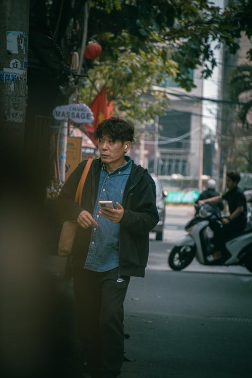 Passerby with Wireless Earphones and a Smartphone in His Hand Walking Down the Street