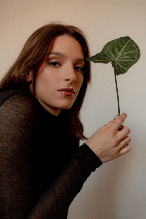 Free Elegant portrait of a woman in black holding a leaf against a white backdrop, showcasing modern aesthetic. Stock Photo