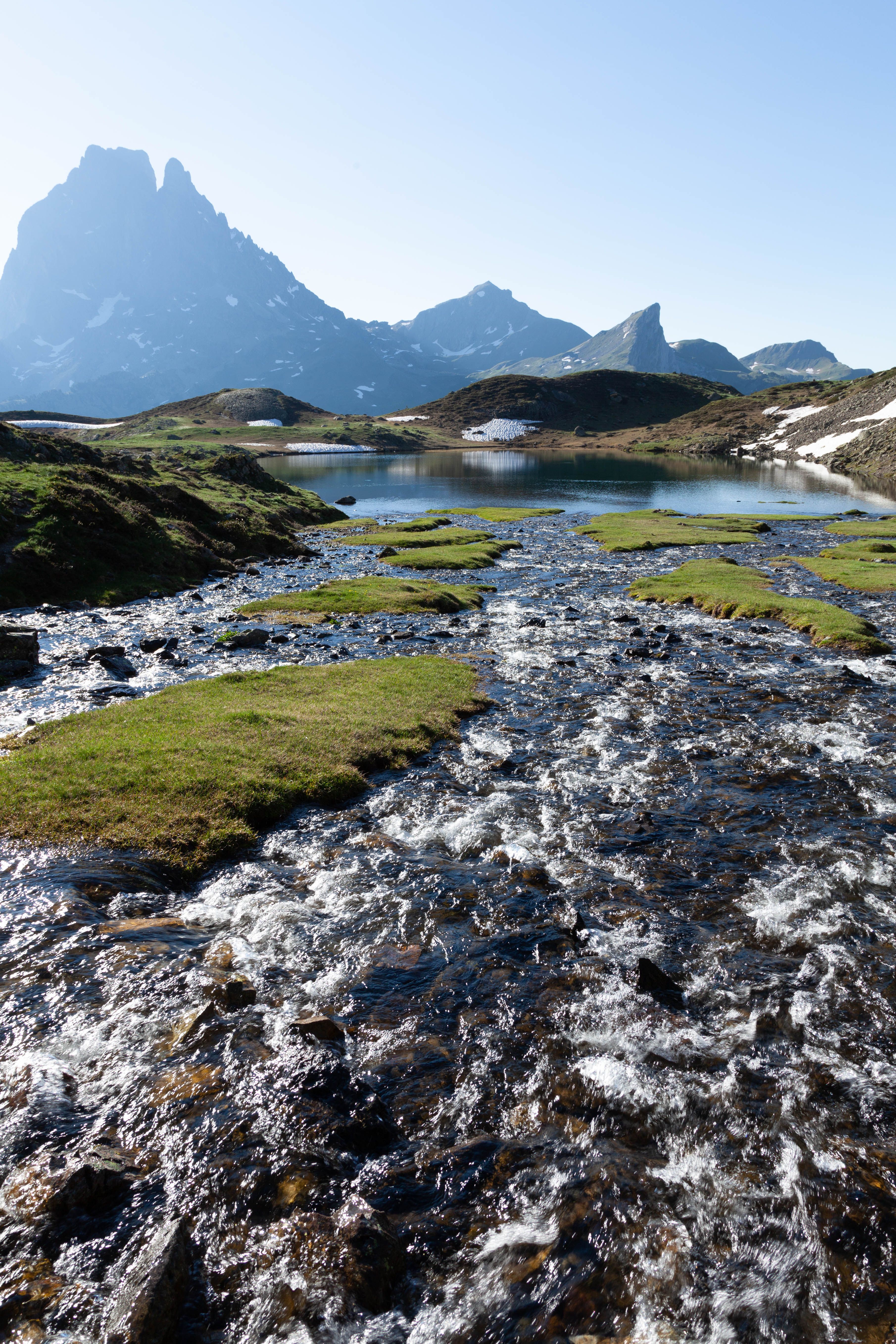 A stream flowing through a grassy field with mountains in the ...