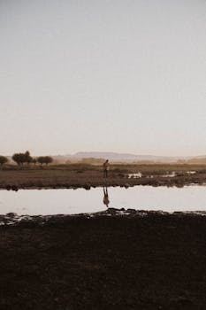 Tranquil rural scene at dusk with a lone figure reflected in a quiet riverbank.