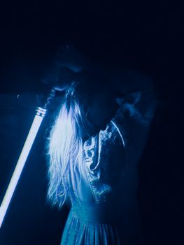 A dramatic portrait of a woman holding a blue lightsaber, casting ethereal illumination in a dark setting.