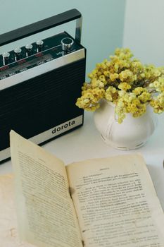 Retro radio with open book and vase of yellow flowers in a still life composition.