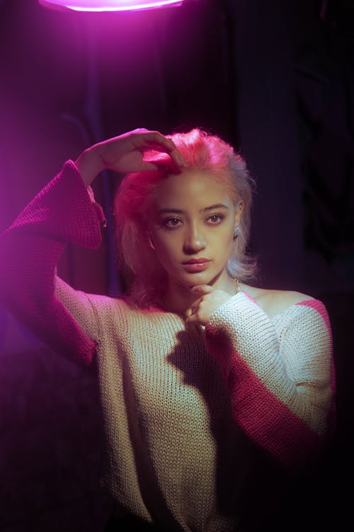 Photo of a Young Woman in a Sweater Posing in Purple Lighting 