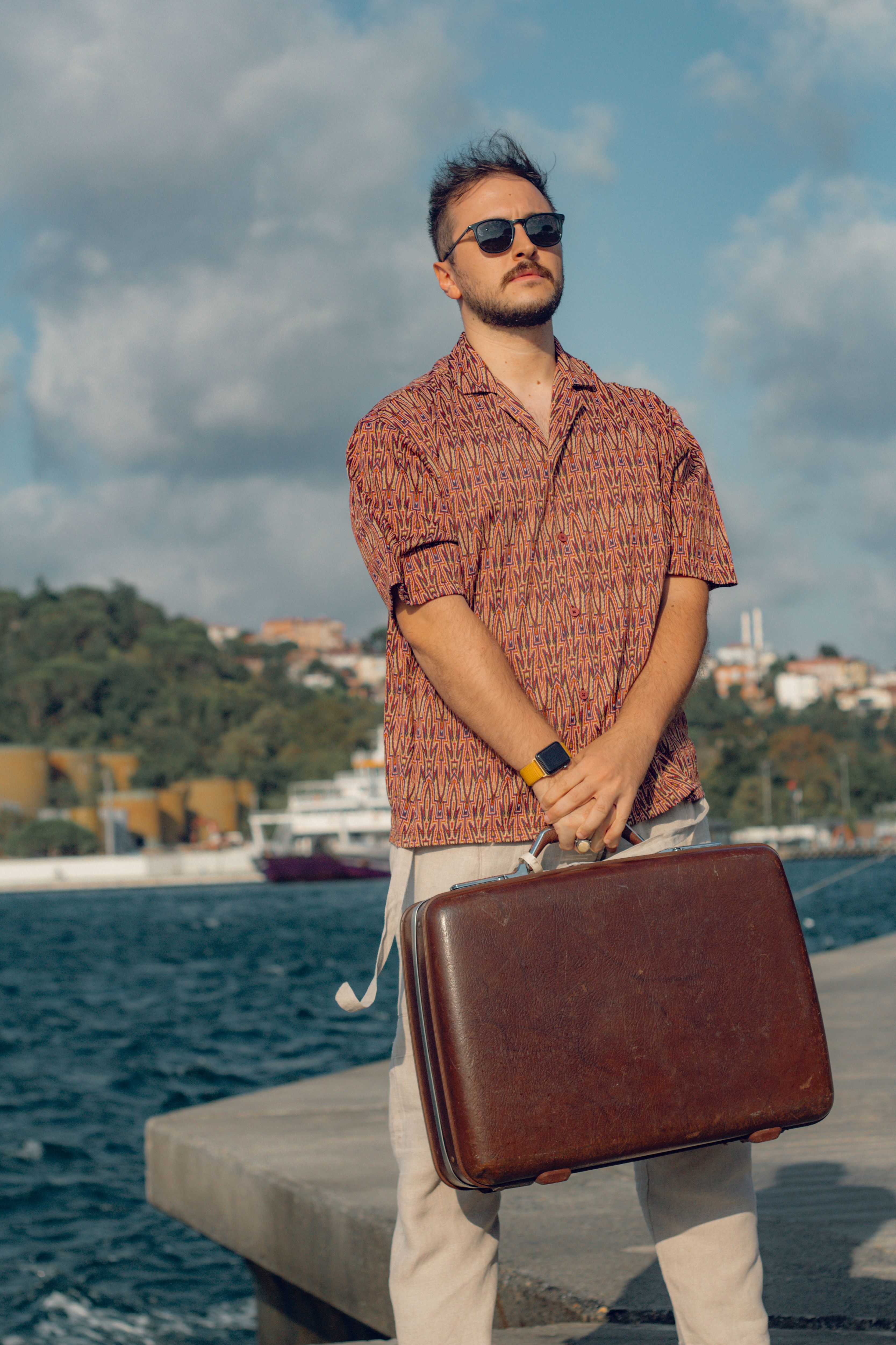 Casual young man in İstanbul port holding suitcase under summer sun.