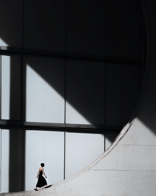 Free A woman walking near the iconic geometry of Berlin's modern architecture, creating a dramatic silhouette in sunlight and shadow. Stock Photo