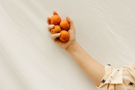 A hand holding fresh oranges on a pale linen backdrop — photo by Jonathan Borba on Pexels