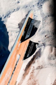 Close-up of surfboard fins partially buried in white sand on a sunny beach day.