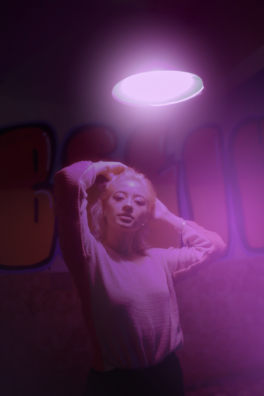 A young woman poses under a vibrant purple light in an urban setting in Ciudad de México.