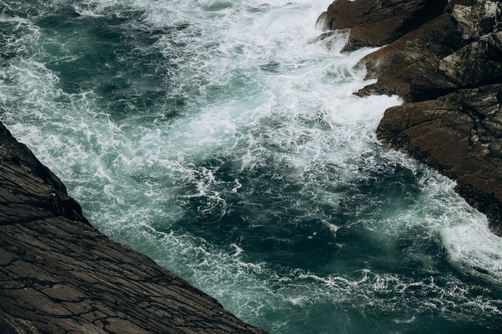 A powerful view of ocean waves crashing against the rugged rocky coastline at Mizen Head, Ireland