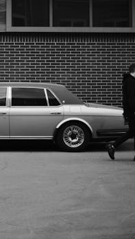 Black and white shot of a classic car against a brick wall with a passerby.
