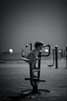 Black and white photo of a child playing on outdoor gym equipment at night in Istanbul.